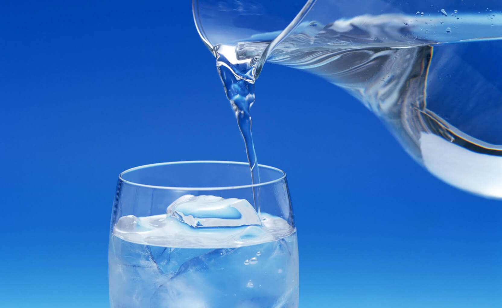 Pouring a jug of water into a glass of water with ice
