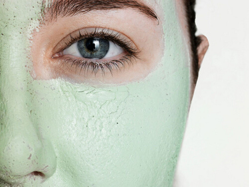 Young woman wearing green facial mask, close-up of eye