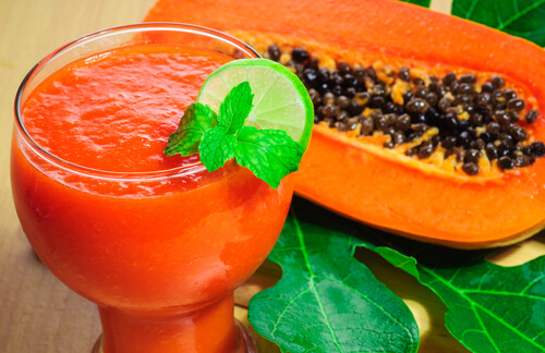 A glass of papaya juice with a piece of papaya next to it