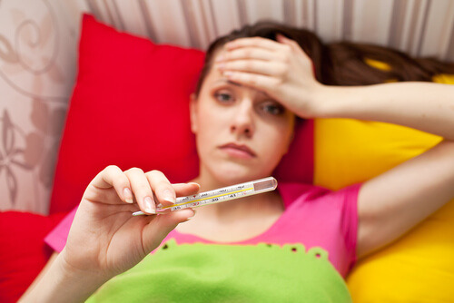 Woman with a fever holding a thermometer