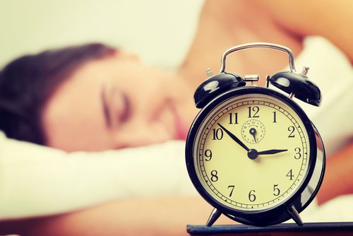Woman sleeps with alarm clock in foreground sleep poorly