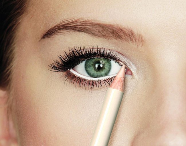 Woman applying white eyeliner to her waterline