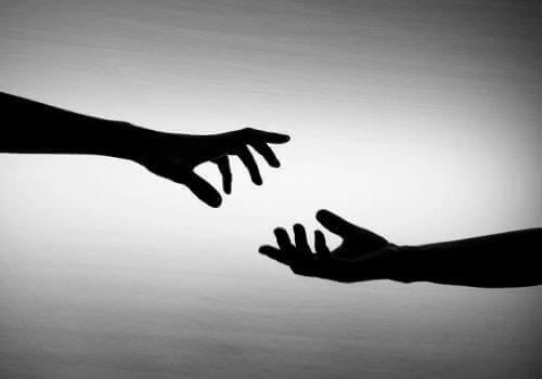 Two hands in shadow reach for each other in the light before dying connection with loved ones