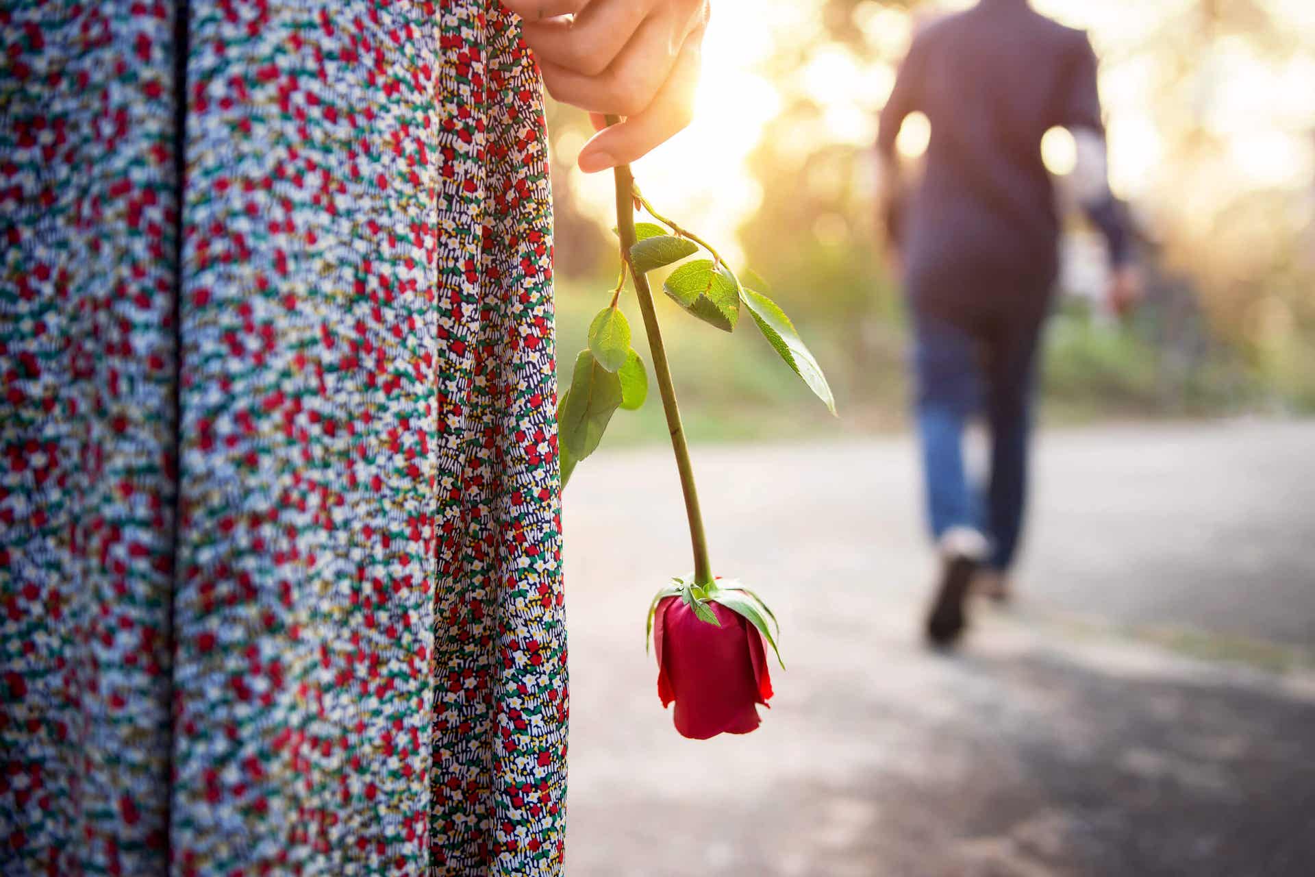 A man walking away from a woman holding a rose down by her side.