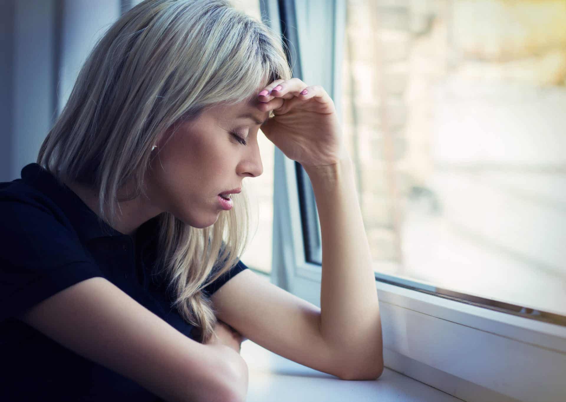A woman leaning on a window sill, looking sad and stressed.
