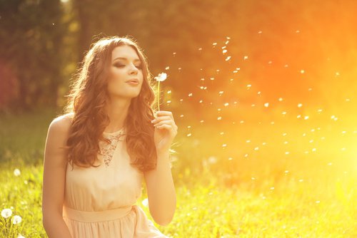 A woman blowing a dandelion in the fields.