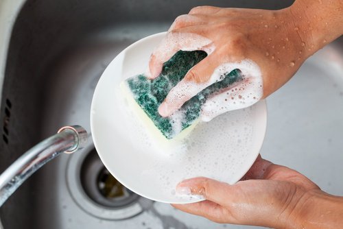 A person washing plates with detergent.
