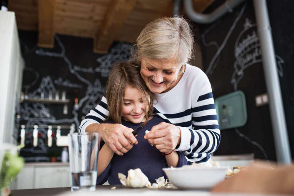A grandmother teaching her granddaughter to cut vegetables.