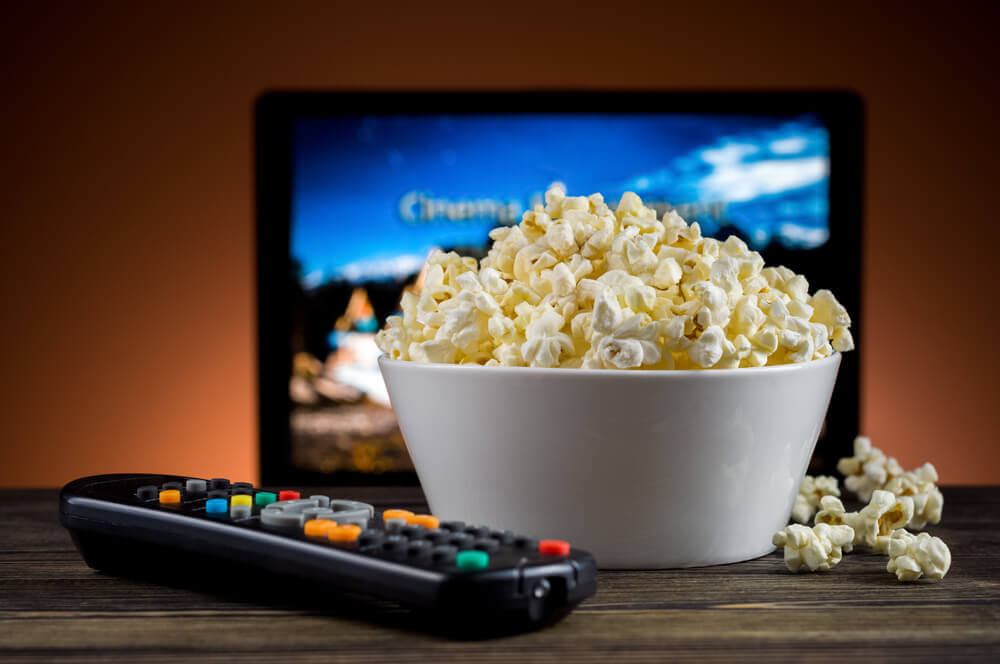 A bowl of popcorn, a remote control, and a TV.