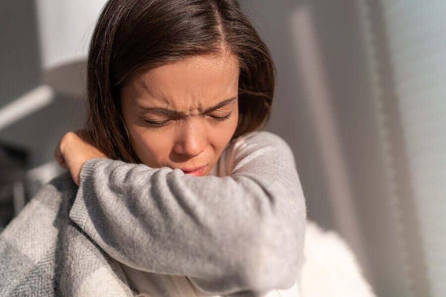 A woman sneezing into her elbow.