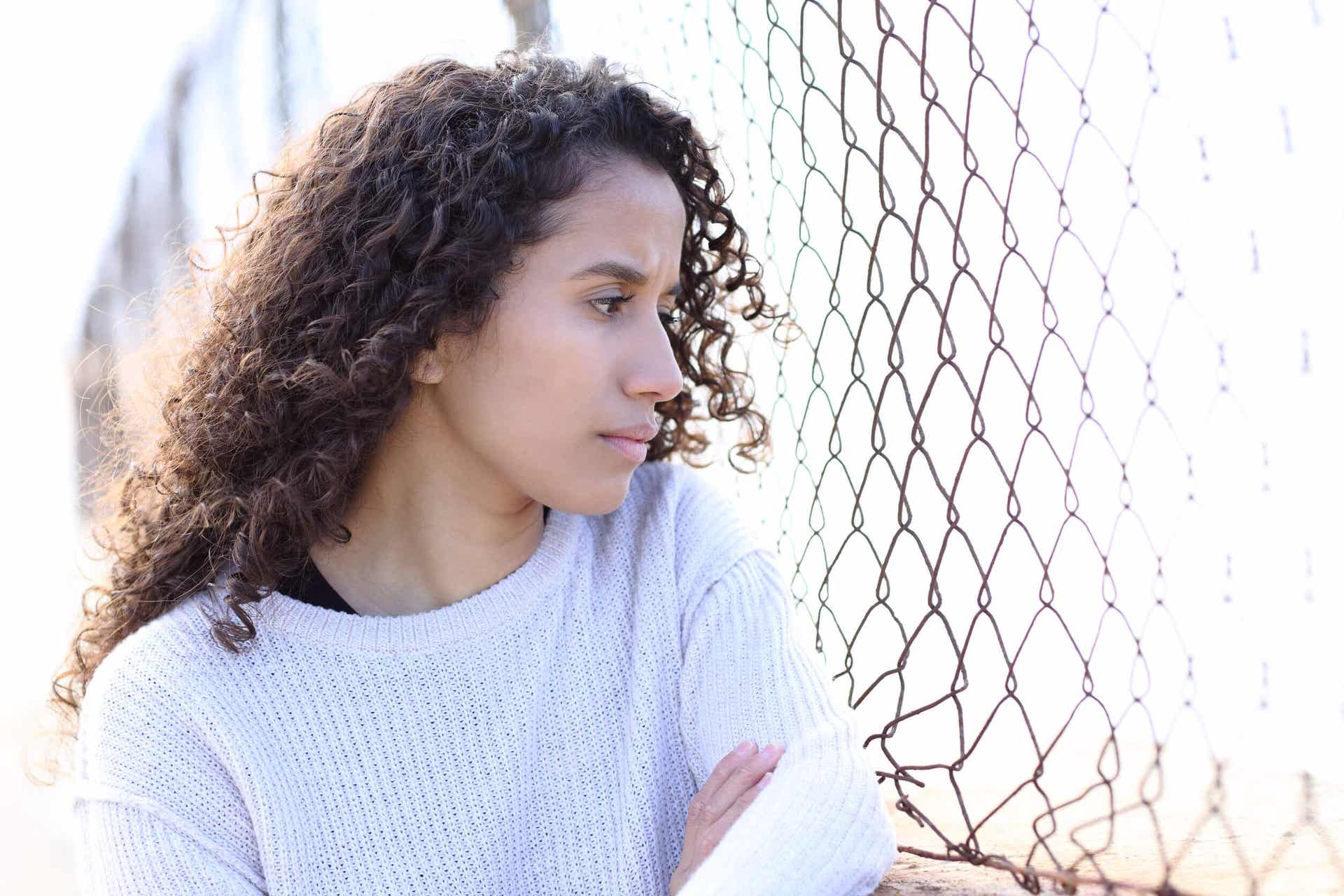 A woman leaning against a fence, looking thoughtful.