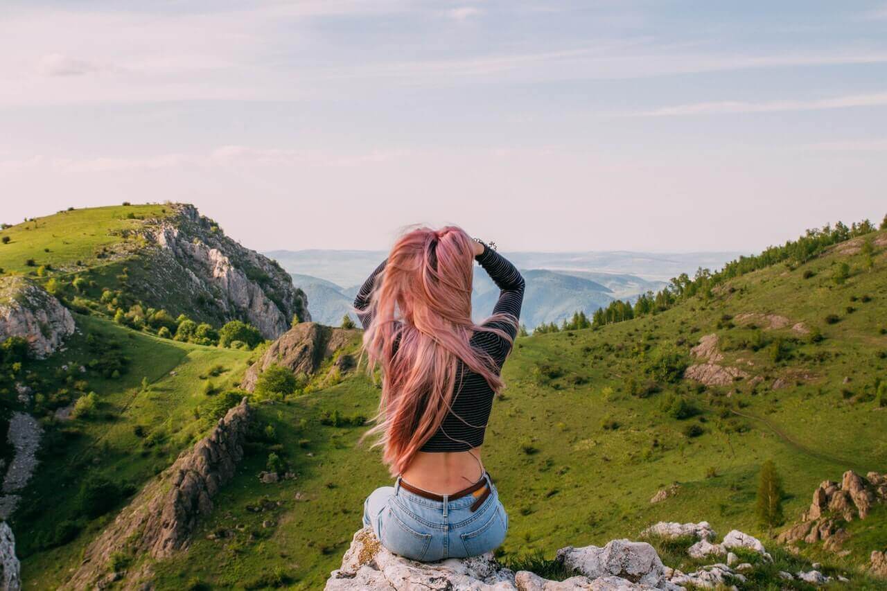 A woman sitting on a rock, looking out at the mountains.