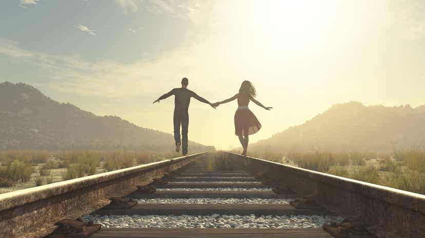 A couple holding hands while walking down a railroad track.