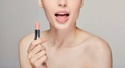A woman applying light pink lipstick.