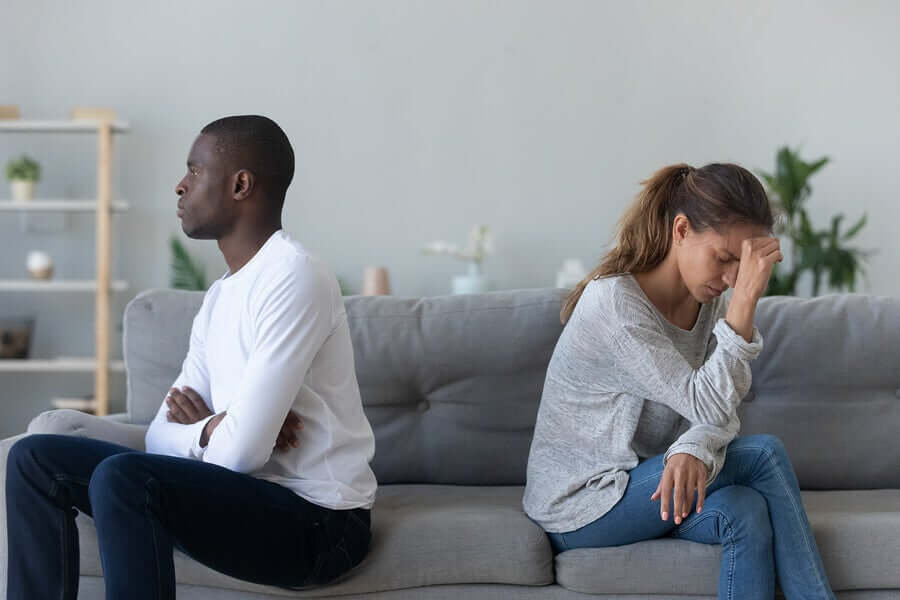 A man and woman sitting on the couch with their backs to one another, looking angry.