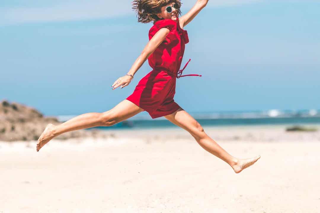 A woman leaping across the sand on the beach.
