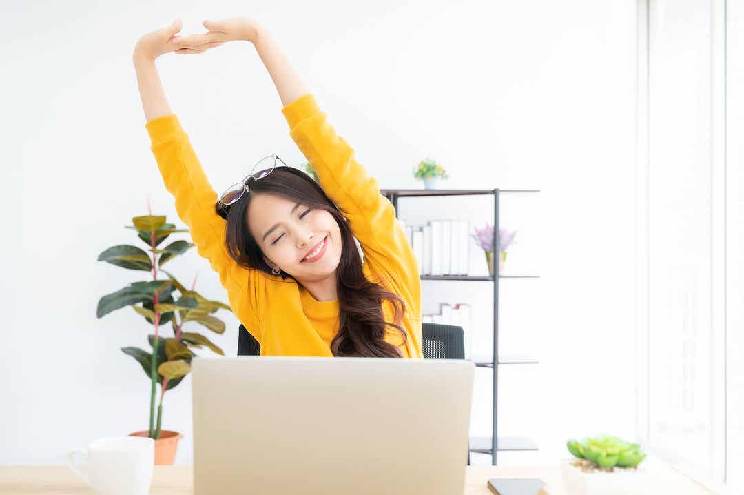 A woman stretching her back while working at her desk.