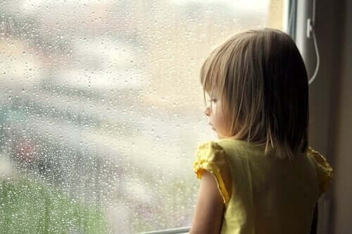 A toddler looking out a window at the rain.