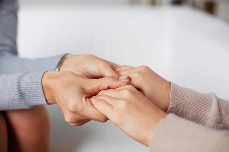 A woman taking another woman's hands in hers, empathetically.