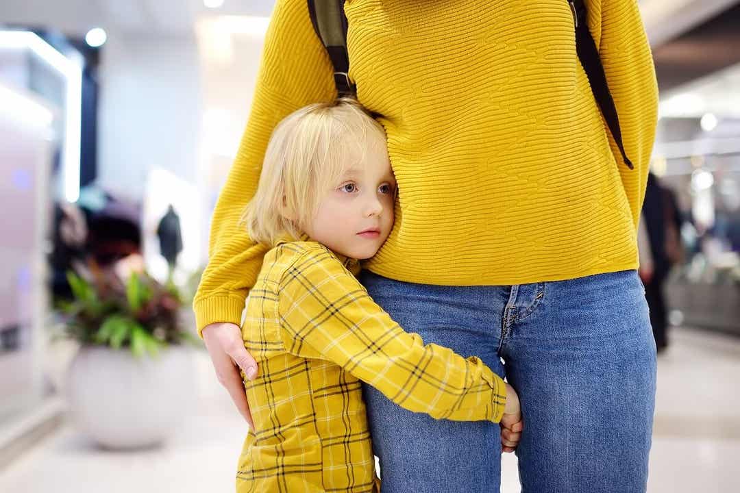 A shy child hugging his mom's leg.