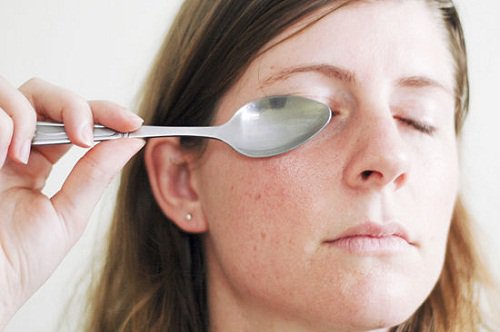 woman holding a spoon over eyelid