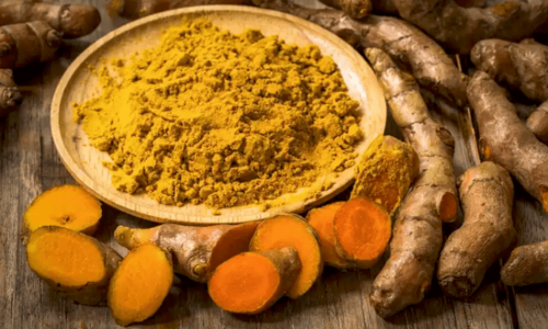 A bowl of powdered turmeric surrounded by roots.