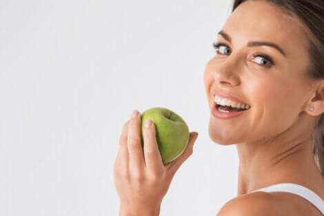A smiling woman holding a green apple.