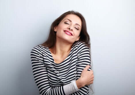 A smiling woman hugging herself.