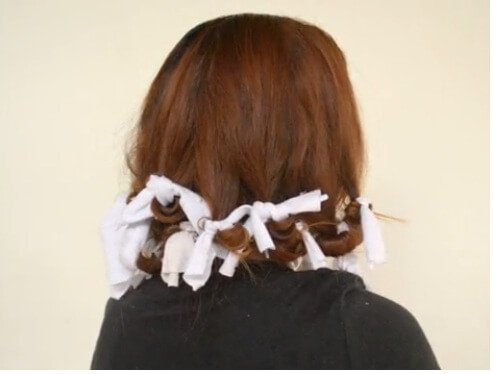 Woman curling her hair with a tee shirt.