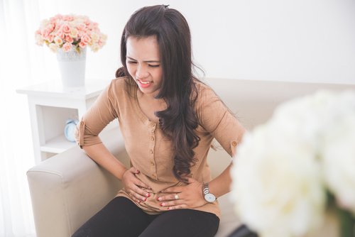 Woman on couch touching abdomen in pain fight digestive problems