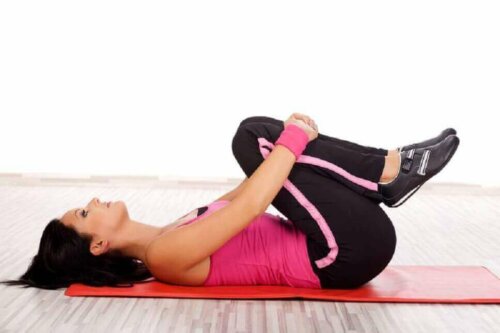 A woman bringing the legs up to her chest to get rid of abdominal fat.