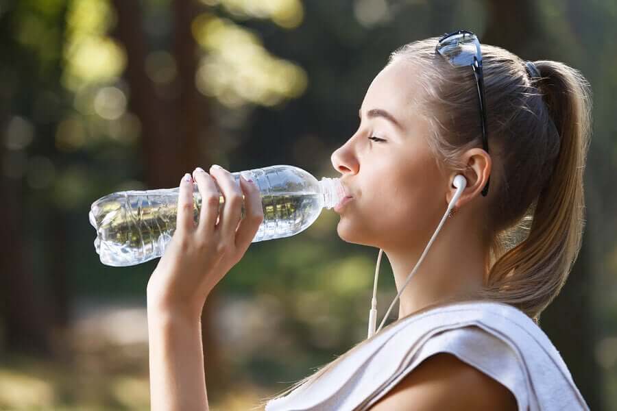 A young woman drinking water while she exercises.