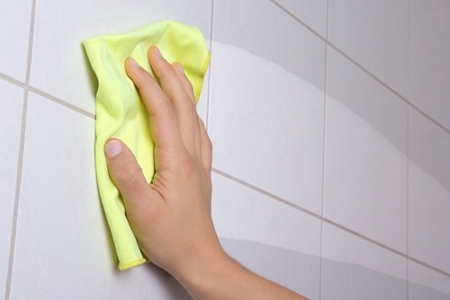 Person cleaning bathroom tiles with a yellow cloth disinfect every day