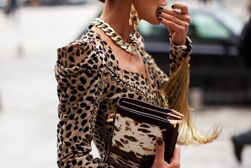 Woman in street eating something and wearing necklace, animal print jacket and carrying animal print purse fashion mistakes