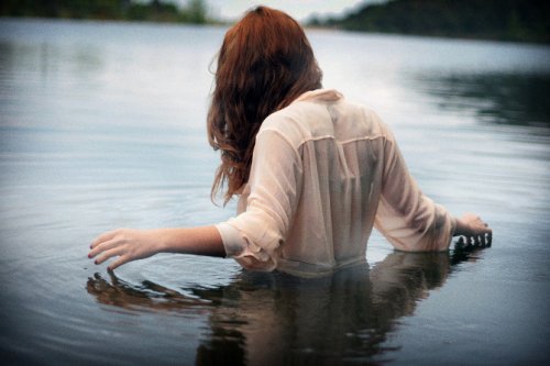 Woman dressed in a white button down shirt wading in a lake accept your present situation