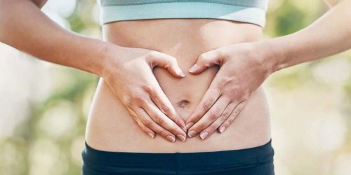 A woman making a heart with her hands on her belly.