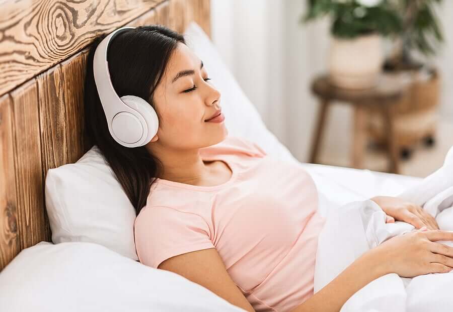 A woman with headphones listening to relaxing music in her bed.