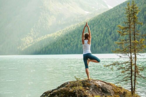A woman reaping the emotional benefits of yoga by the lake.