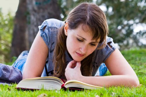 Tyttö makaa nurmikolla lukemassa kirjaa.