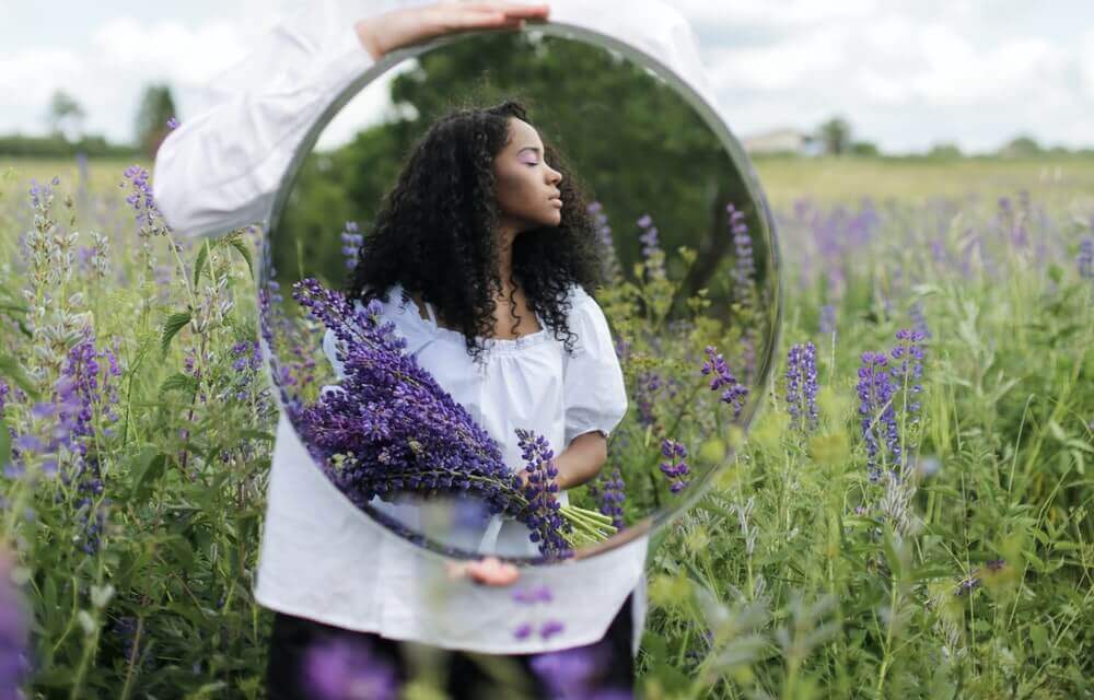 A mirror reflecting a woman standing in a lavender field, holding a boquet.