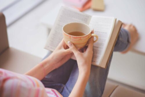Osoba czytająca książkę i pijąca herbatę.