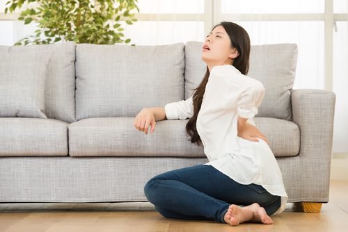 A woman siting on the ground presses her hand against her lower back in pain