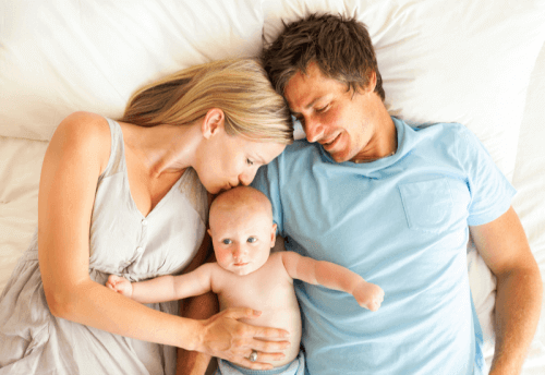 parents laying in bed with their baby