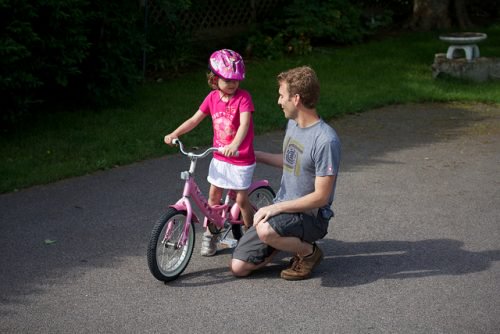 Father teaching daughter to ride a bike on driveway strong woman