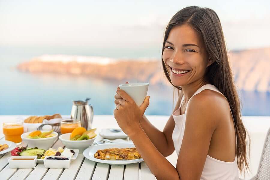 A woman eating a healthy meal at a table overlooking the ocean.