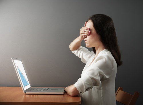 Woman covering her eyes in front of a computer