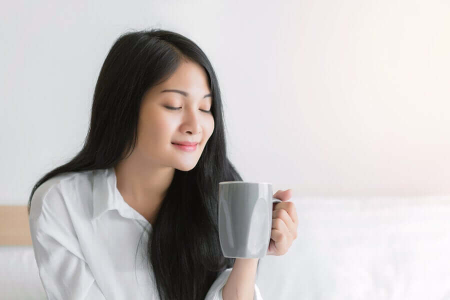 A woman holding a cup of tea with her eyes closed.