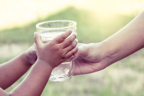 A child giving a glass water to an adult.