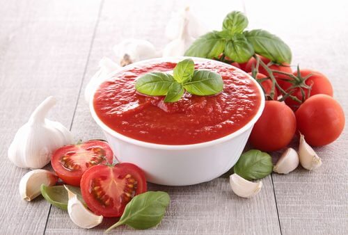 Bowl of tomato sauce on a table with tomatoes, garlic, and basil.