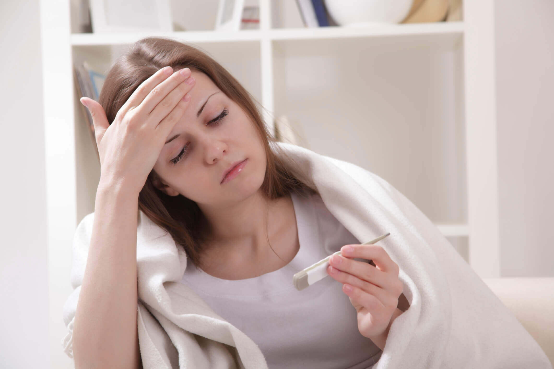 sick woman taking her temperature with a thermometer
